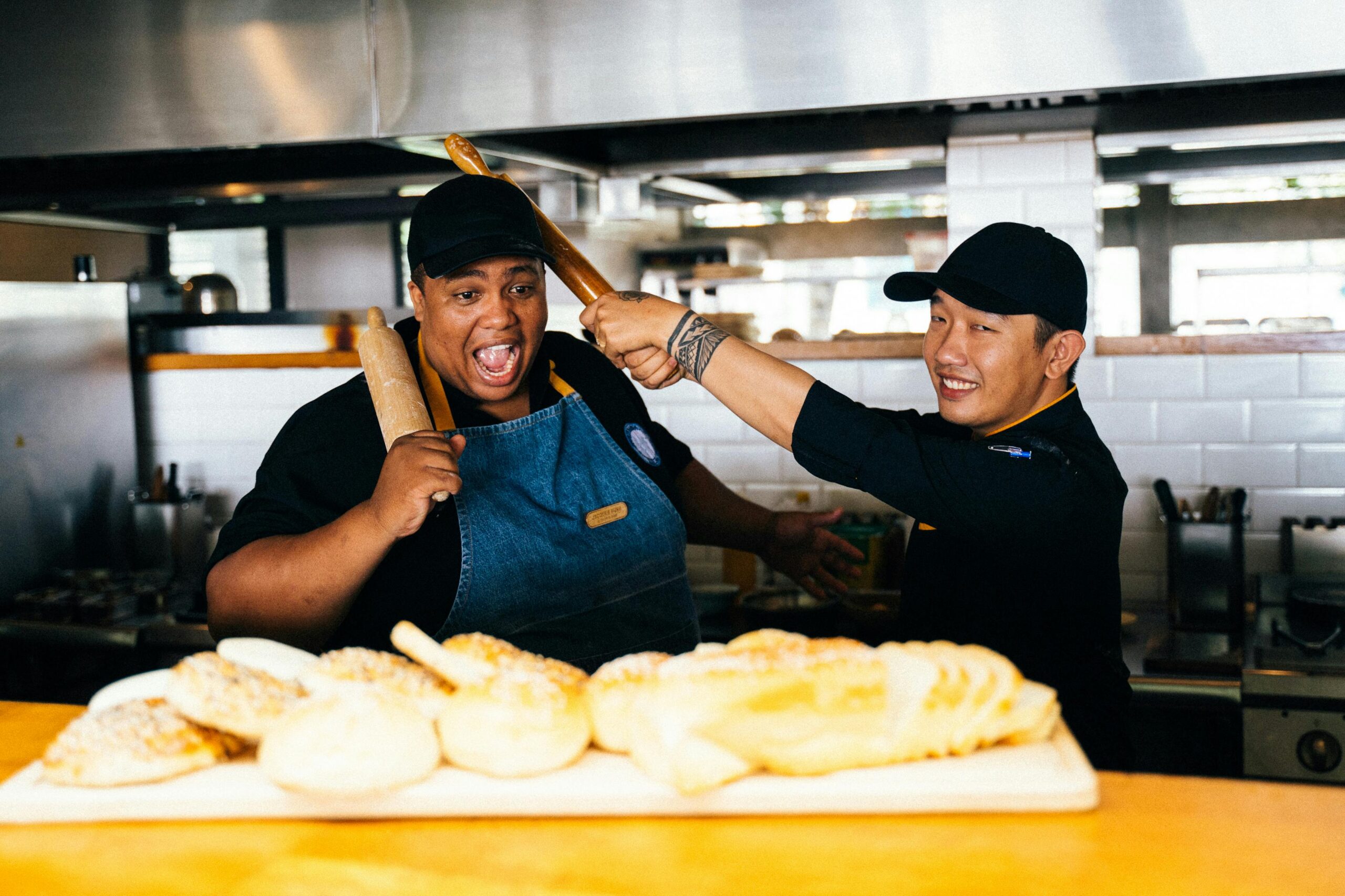 Two cheerful bakers having fun with bread in a lively kitchen setting.