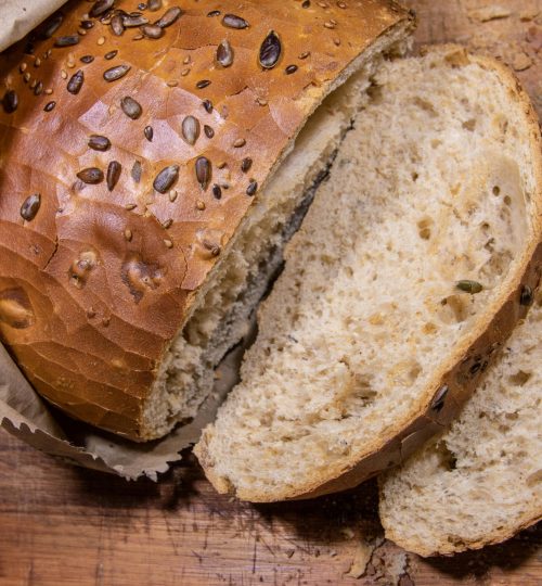 Close-up of sliced brown seeded bread on a rustic wooden cutting board with a paper bag.