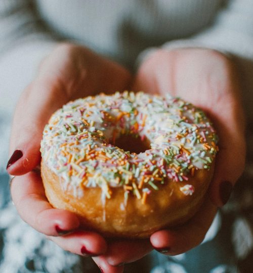 Close-up photo of a donut with colorful sprinkles held in hands, ideal for food and indulgence themes.