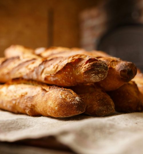 Warm, freshly baked rustic baguettes stacked in a cozy bakery setting.