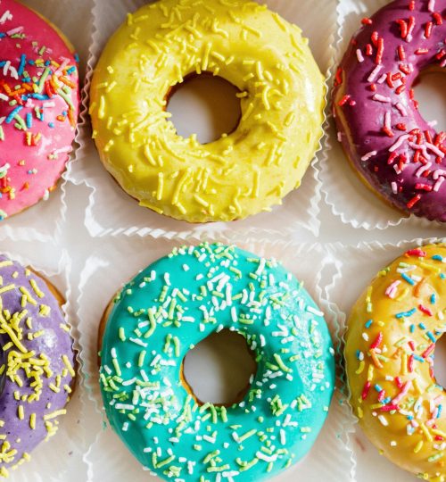 Assorted colorful glazed donuts with sprinkles arranged in a flat lay.