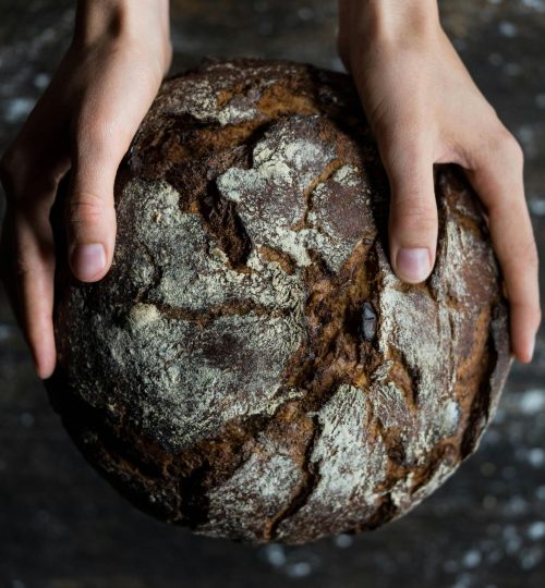 Close-up of hands holding a rustic loaf of whole wheat bread with a dark, textured crust.