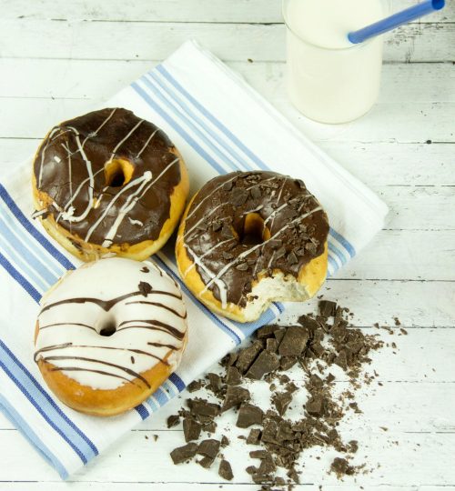 Indulgent chocolate donuts with milk presented on a rustic wooden table, perfect for dessert lovers.